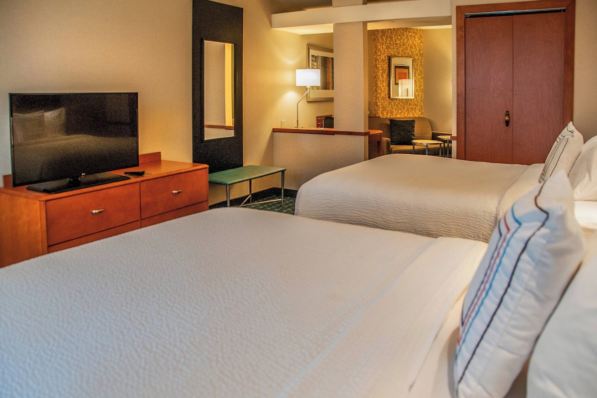 A hotel room with two beds, a TV, a desk, and a mirror.