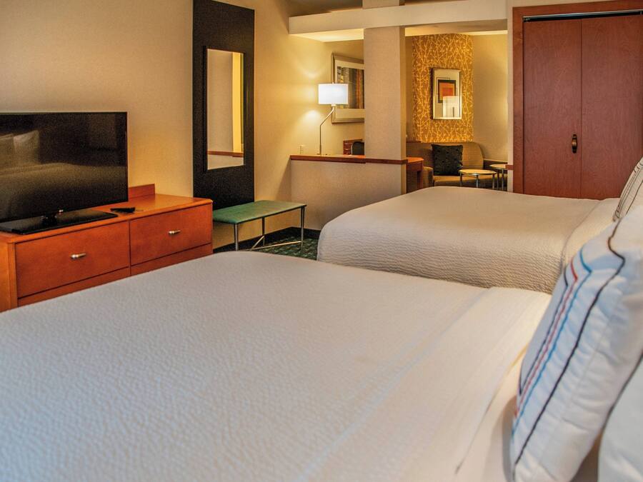 A hotel room with two beds, a TV, a desk, and a mirror.