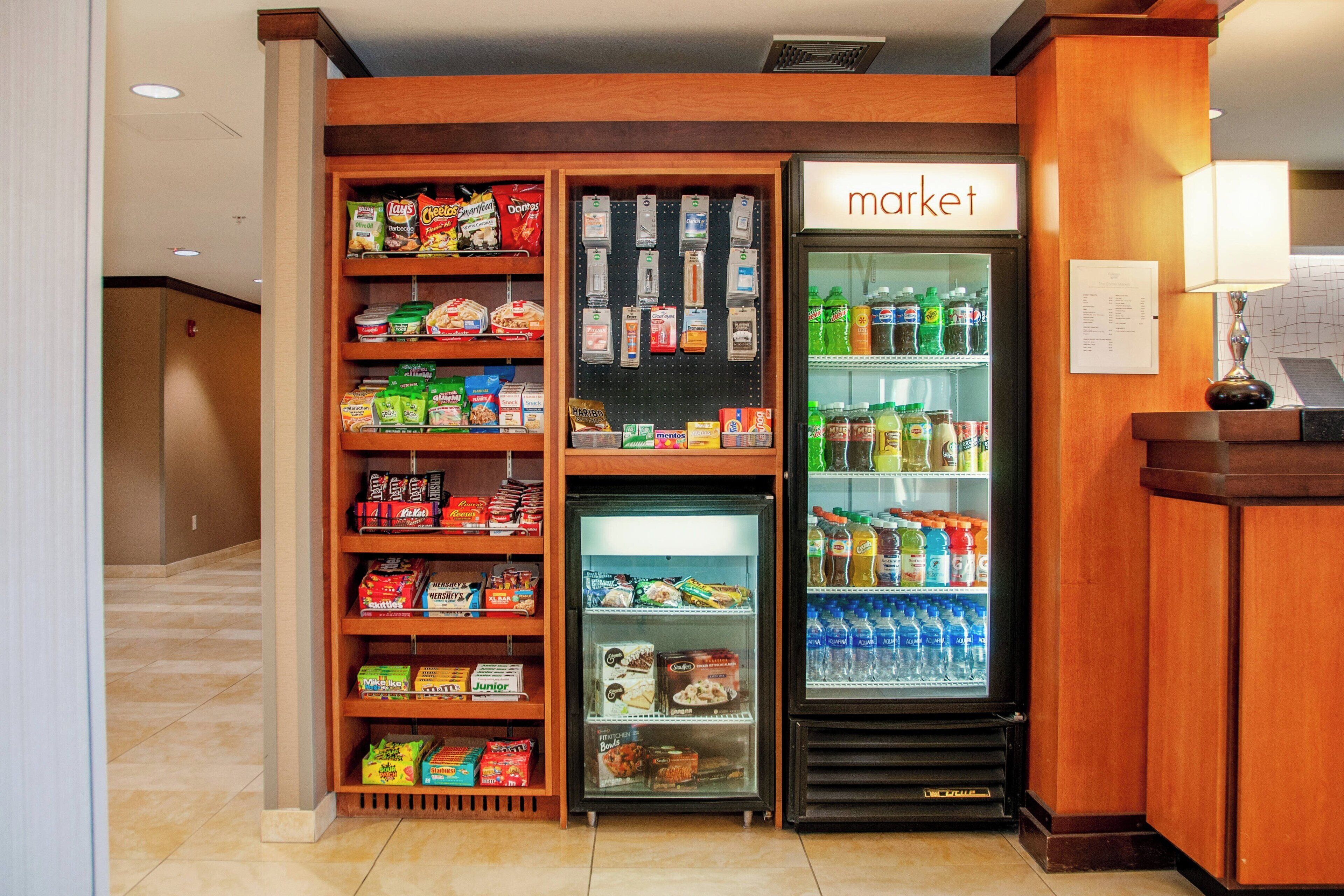 Un hall de hotel con un área de comida autoservicio, que incluye un refrigerador y un congelador llenos de refrigerios y bebidas.