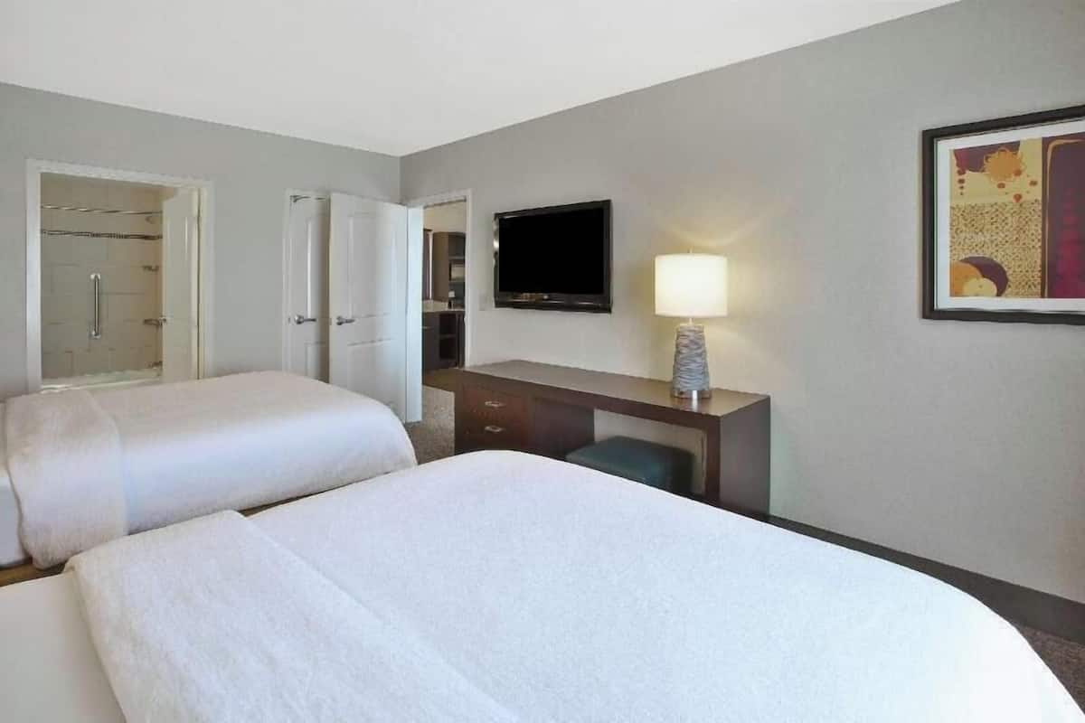 Quarto de hotel com duas camas, uma escrivaninha, uma televisão e um abajur.