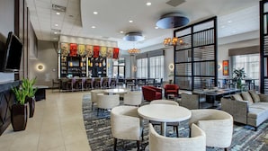A spacious lobby with a bar area, seating arrangements, and a large screen. - Embassy Suites Columbus-Airport (Columbus)