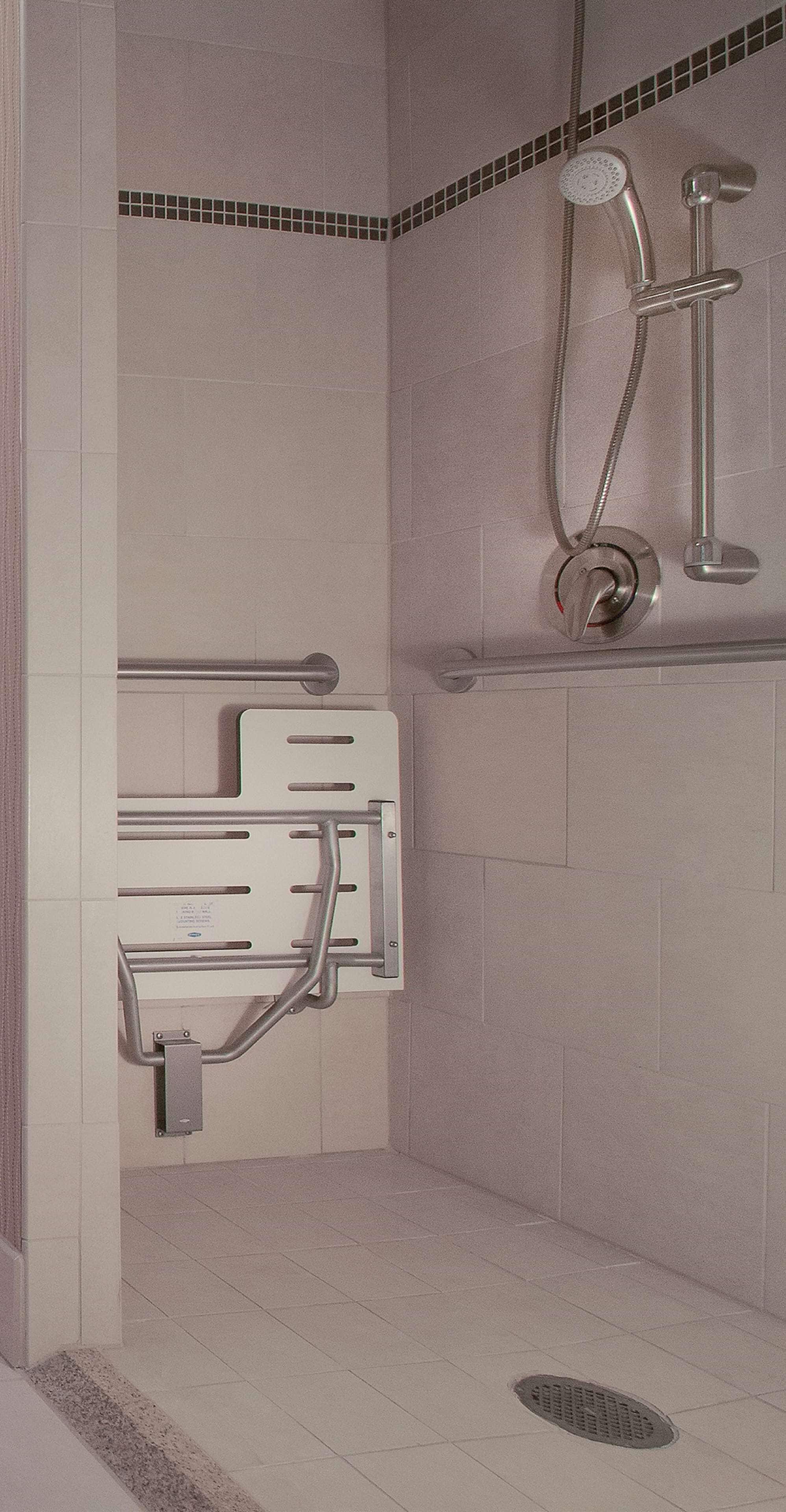 A shower area with a handheld showerhead, a wall-mounted faucet, and a grab bar for support.