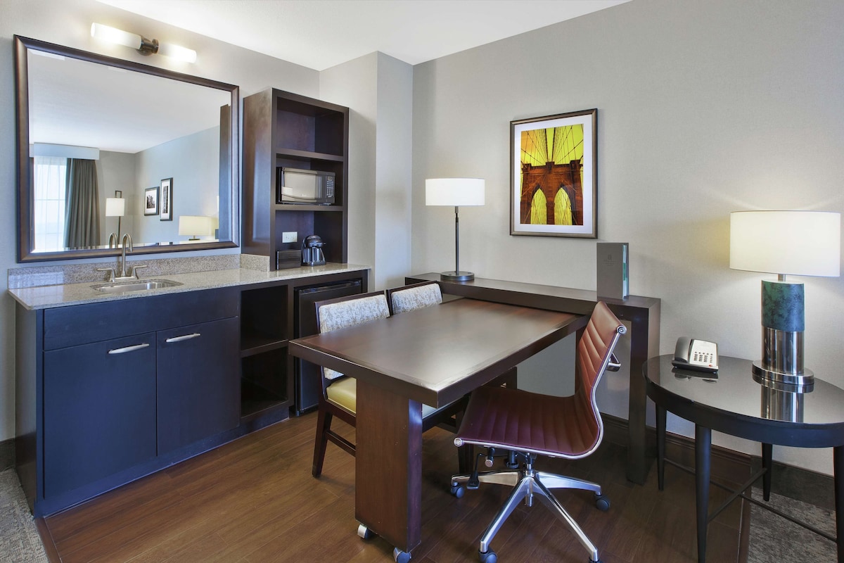 A hotel room with a large mirror, a dining table with chairs, a microwave, a coffee maker, and a telephone.