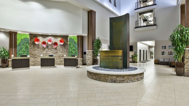 A spacious lobby with a reception desk, a stone wall with greenery, a central water feature, and a balcony with plants. - Embassy Suites Columbus-Airport (Columbus)
