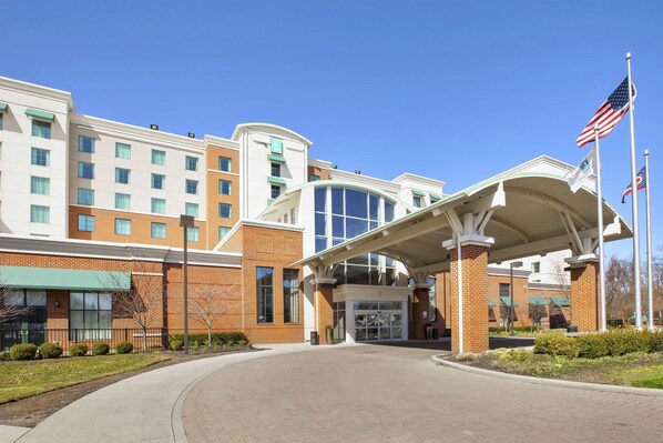 A hotel entrance with a covered walkway, brick facade, and American flags. - Embassy Suites Columbus-Airport (Columbus)