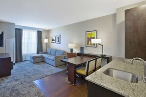A hotel room with a dining area, a sofa, a TV, a lamp, and a sink. - Embassy Suites Columbus-Airport (Columbus)