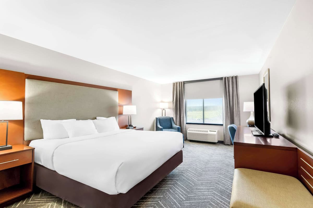 A hotel room with a large bed, a desk with a TV, a chair, and a window with curtains.