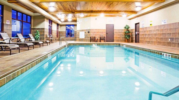 An indoor swimming pool with clear water, lounge chairs, and a wooden ceiling.