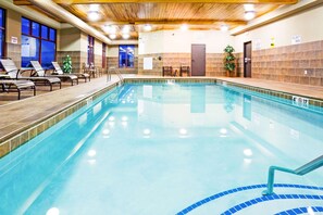 Une piscine intérieure à l’eau claire, dotée de chaises longues et d’un plafond en bois.