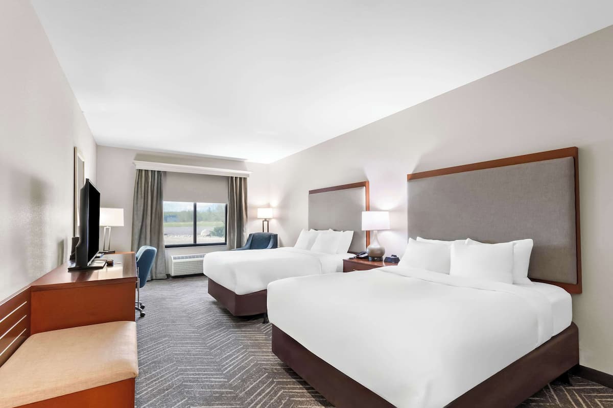 A hotel room with two beds, a desk, a chair, a TV, and a window with curtains.