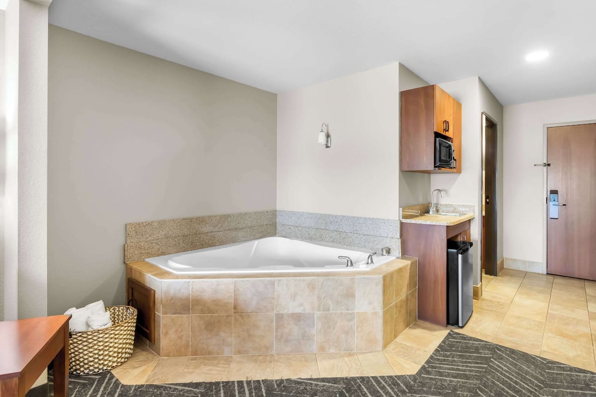 A modern bathroom with a large bathtub, a wooden vanity, and a microwave above it.