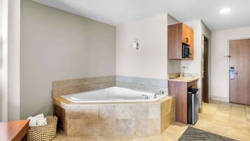 A modern bathroom with a large bathtub, a wooden vanity, and a microwave above it.