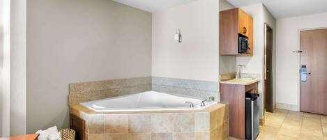 A modern bathroom with a large bathtub, a wooden vanity, and a microwave above it.