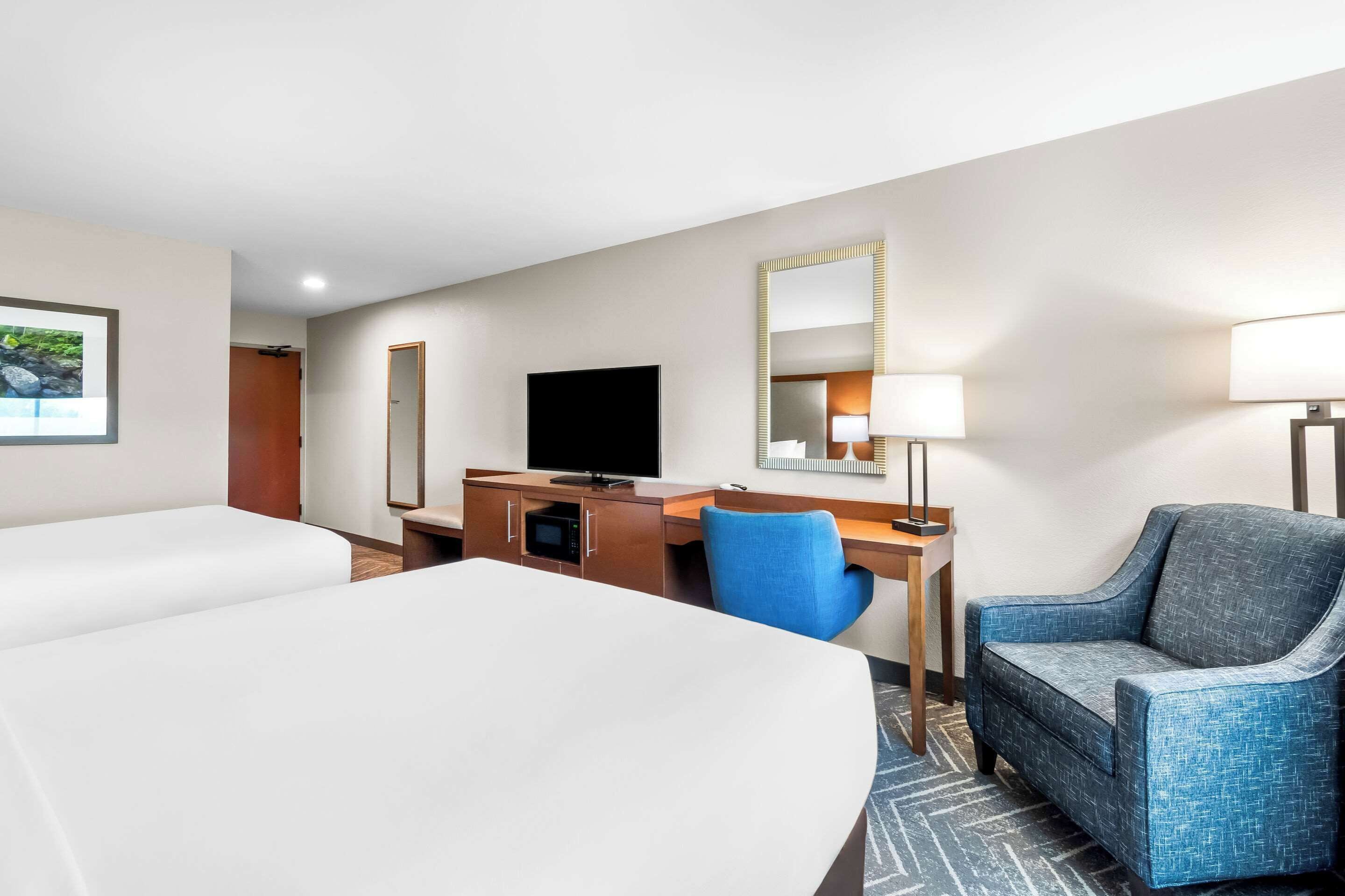 Habitación de hotel con dos camas, un escritorio, una silla, un televisor, un espejo y una lámpara.