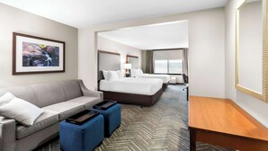 A hotel room with a sofa, two beds, a desk, and a large window.