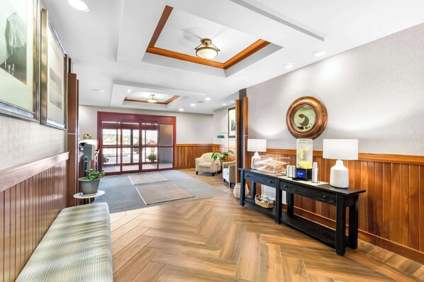 Un hall d’hôtel avec un plancher en bois, un comptoir d’accueil, un banc et une grande horloge au mur.