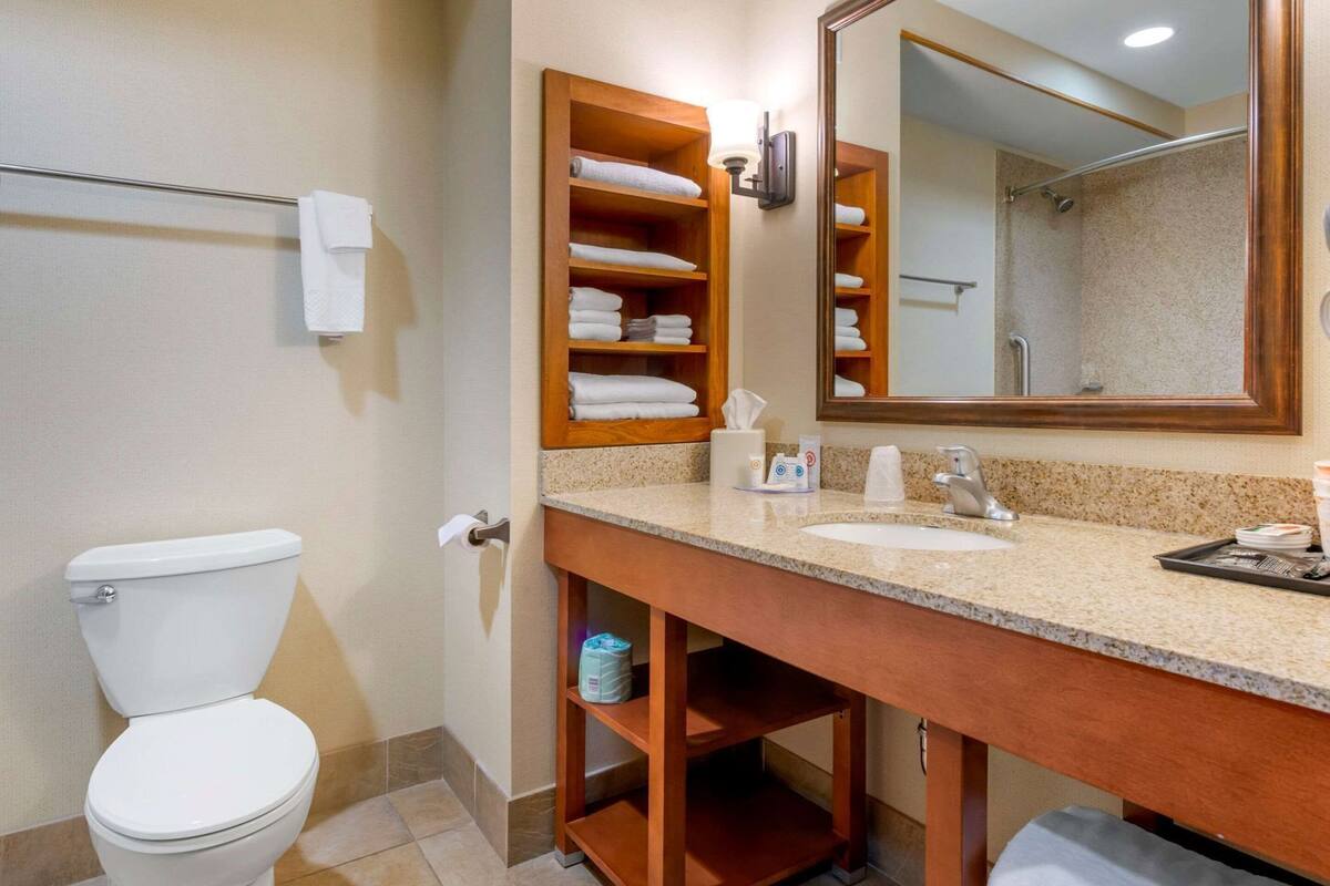 A bathroom with a toilet, sink, mirror, towel rack, and shelves with towels.