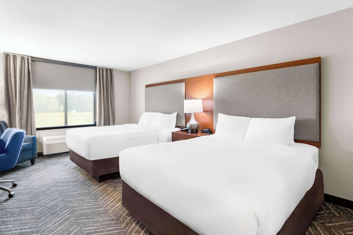 A hotel room with two beds, a desk, a chair, and a large window with curtains.