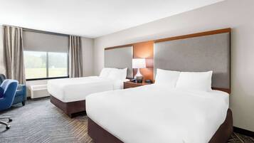 Habitación de hotel con dos camas, un escritorio, una silla y un ventanal con cortinas.