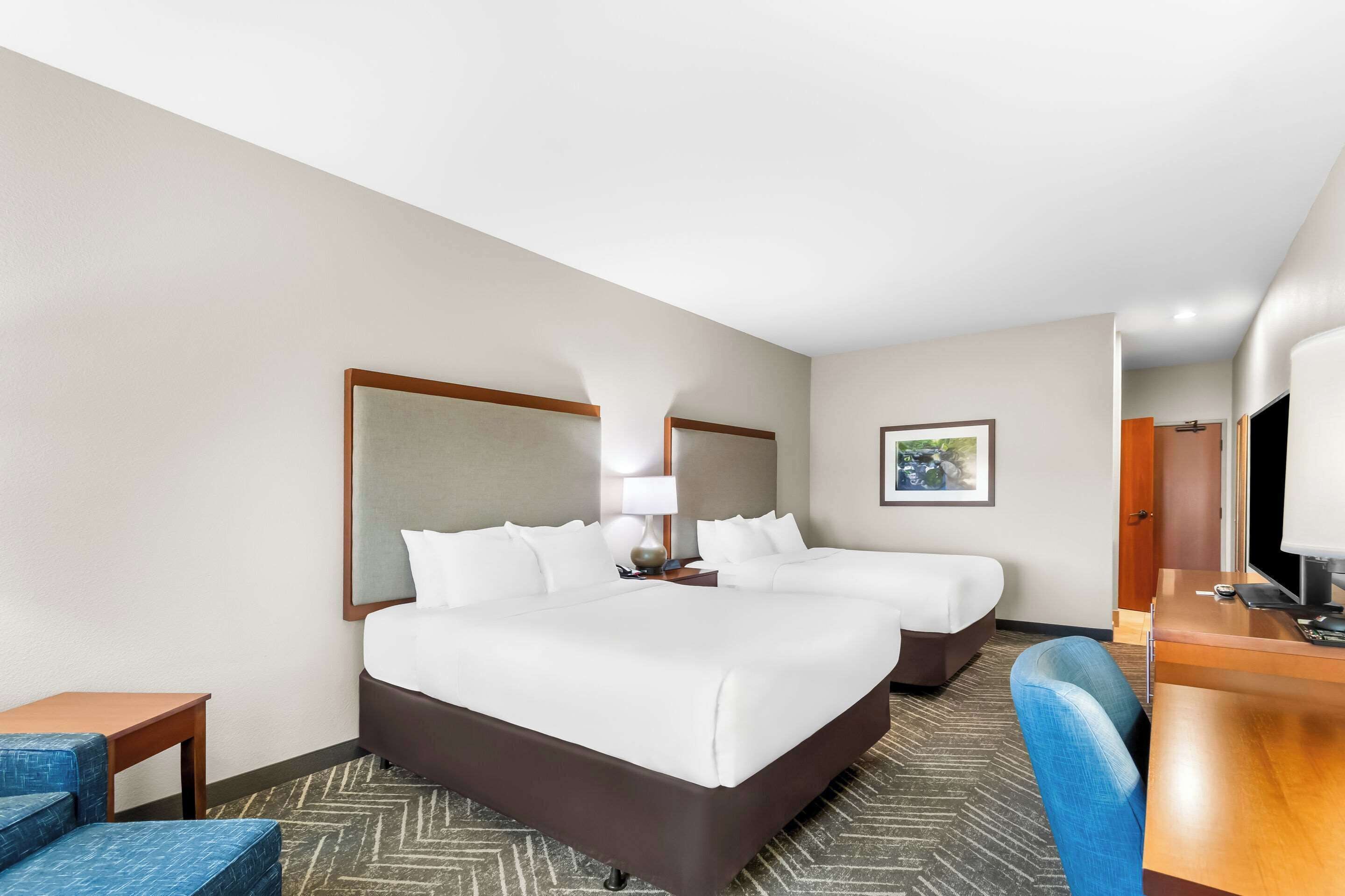 A hotel room with two beds, a desk, a chair, and a television.