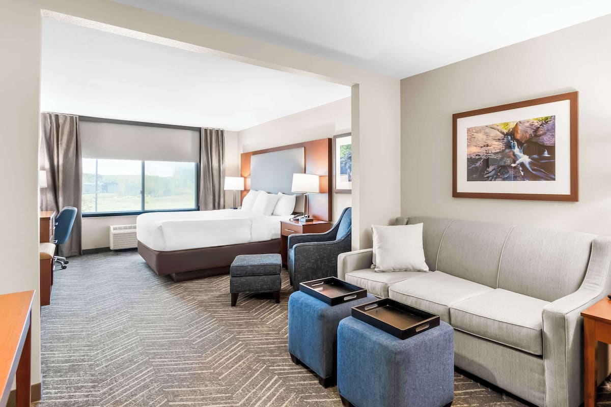 A hotel room with a bed, a sofa, two armchairs, a desk, and a large window.