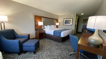 Una habitación de hotel con una cama, dos sillones, un escritorio con lámpara y suelo alfombrado.