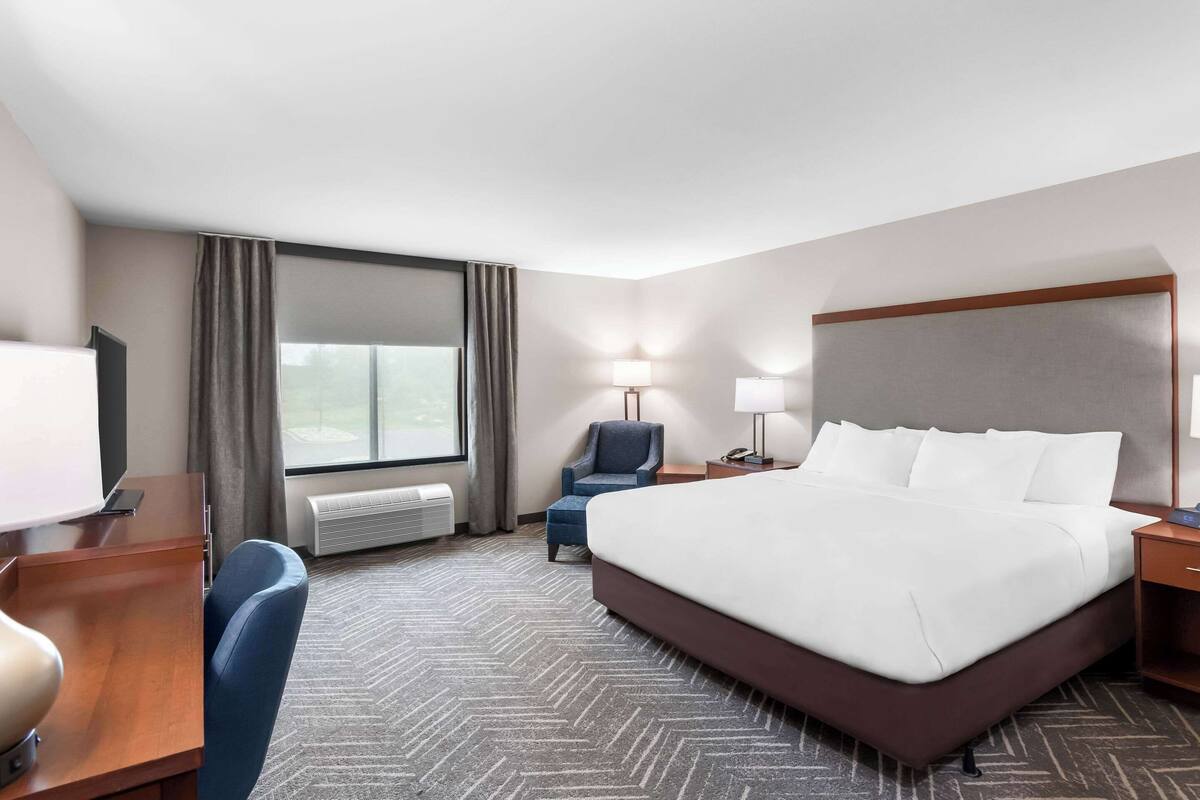 A hotel room with a large bed, a desk, a chair, a TV, and a window with curtains.