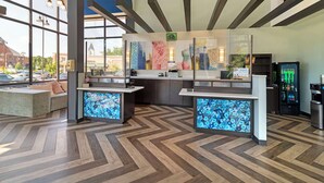 Una zona de recepción moderna con un suelo tipo espiga, grandes ventanales y una recepción con pantalla digital.