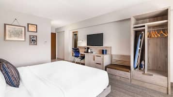 Een hotelkamer met een bed, een bureau, een televisie, een kledingkast en een spiegel.