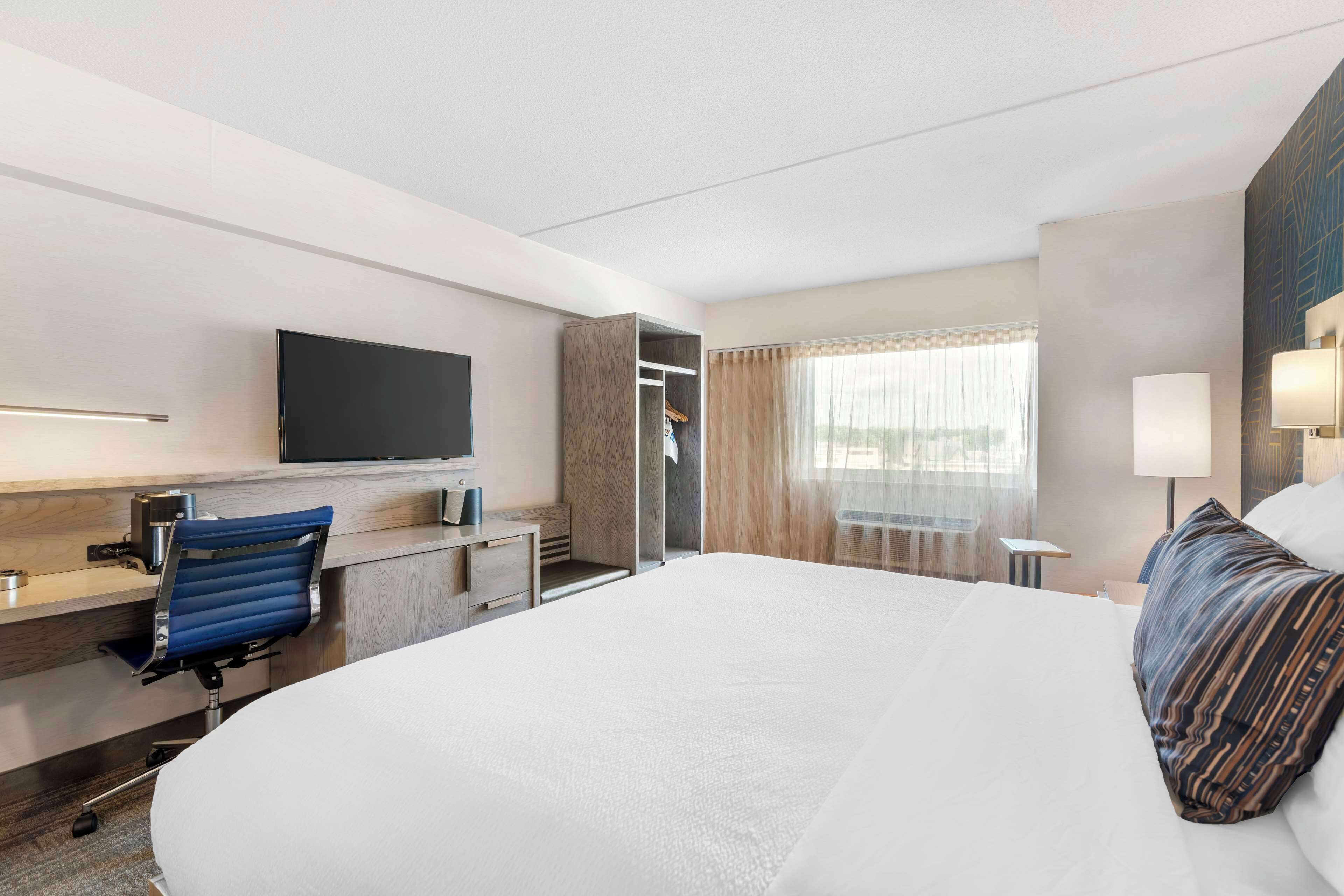 A hotel room with a large bed, a desk with a chair, a television, and a window with curtains.