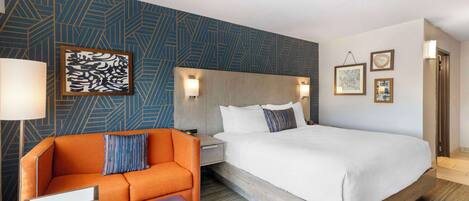 A hotel room with a large bed, a sofa, a desk, and a patterned wall.