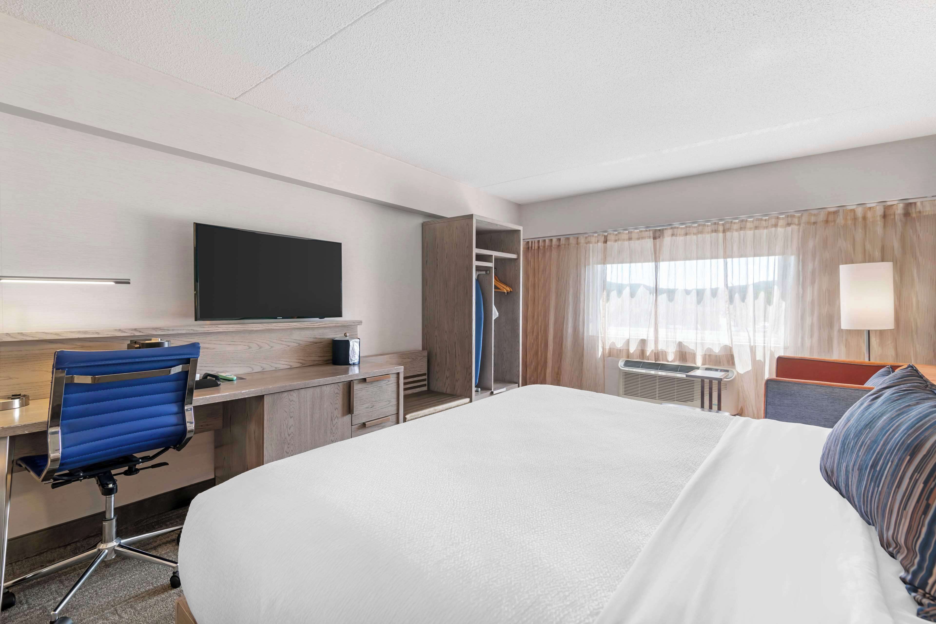 A hotel room with a large bed, a desk with a chair, a TV mounted on the wall, and a wardrobe.