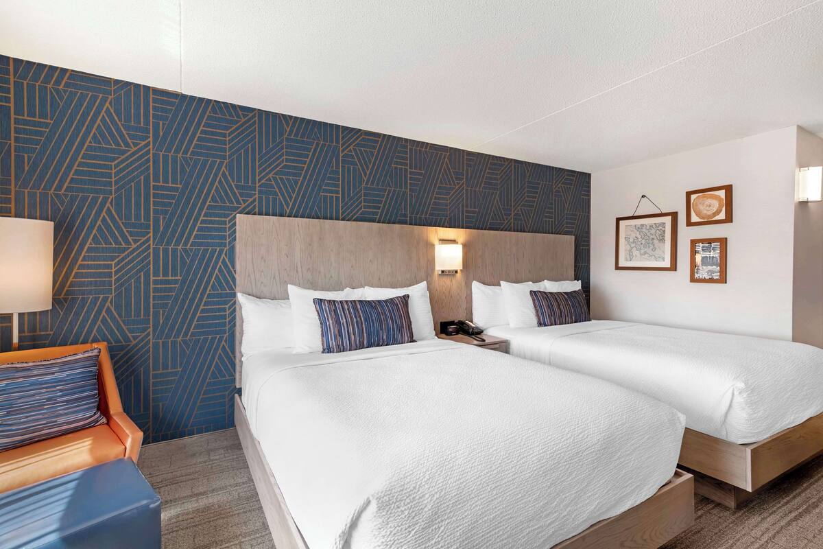 A hotel room with two beds, a wooden headboard, a nightstand, a lamp, and a patterned wall.