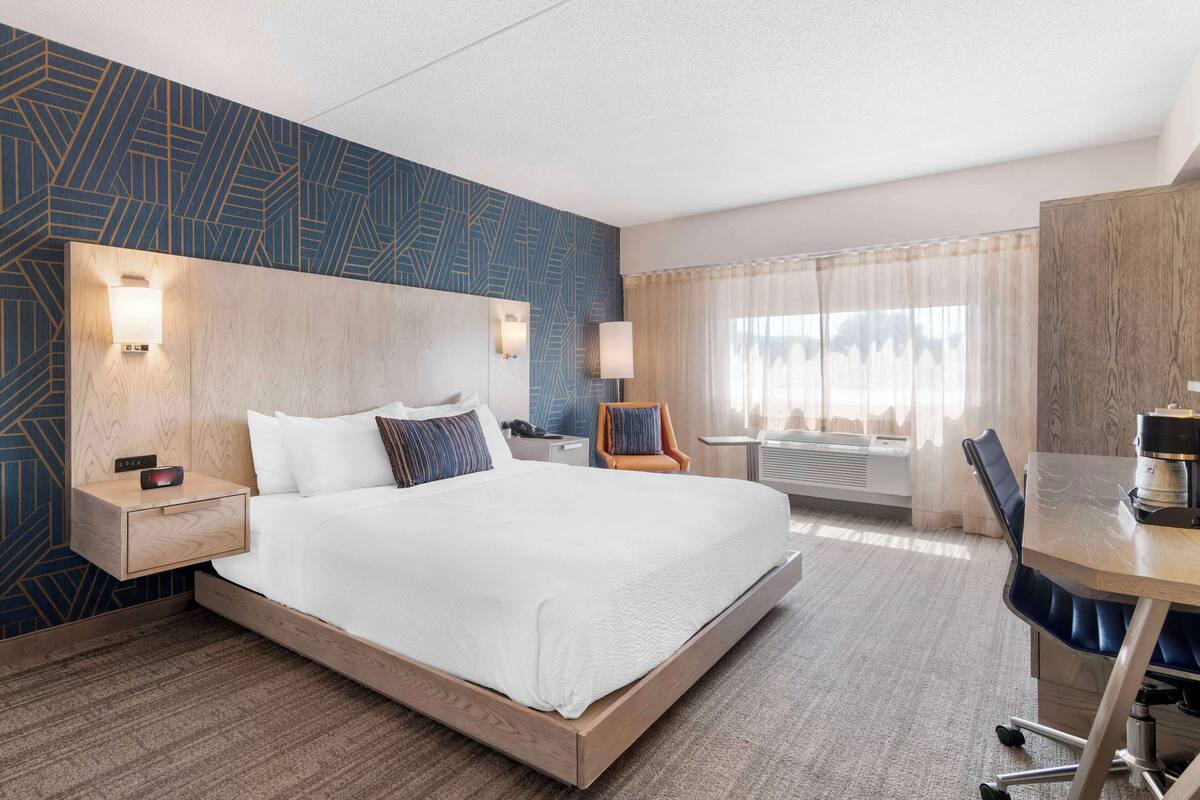 A hotel room with a large bed, bedside tables, a desk, and a chair.