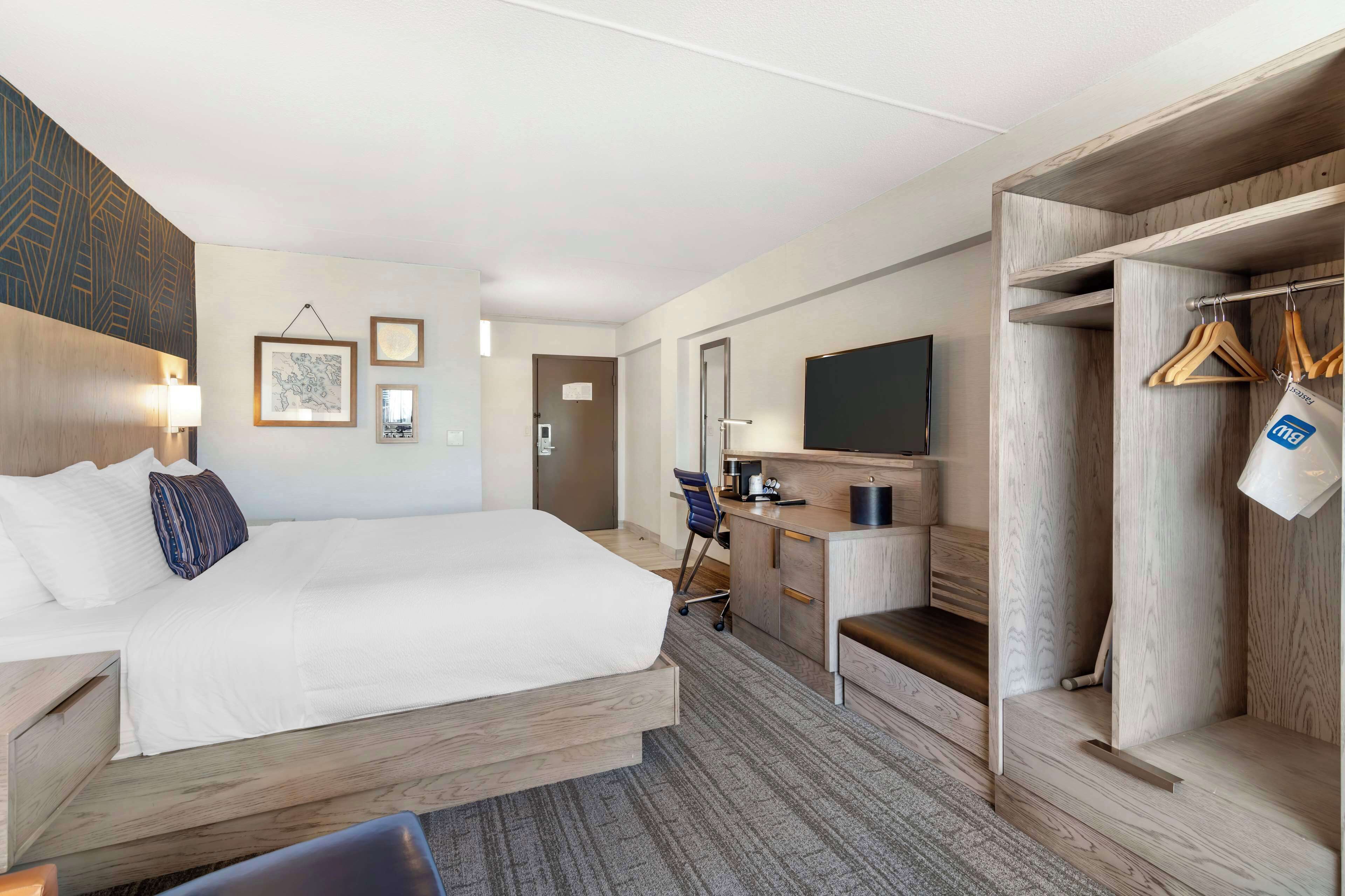 A hotel room with a bed, desk, chair, wardrobe, and a television.