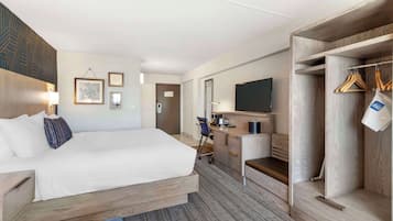 A hotel room with a bed, desk, chair, wardrobe, and a television.