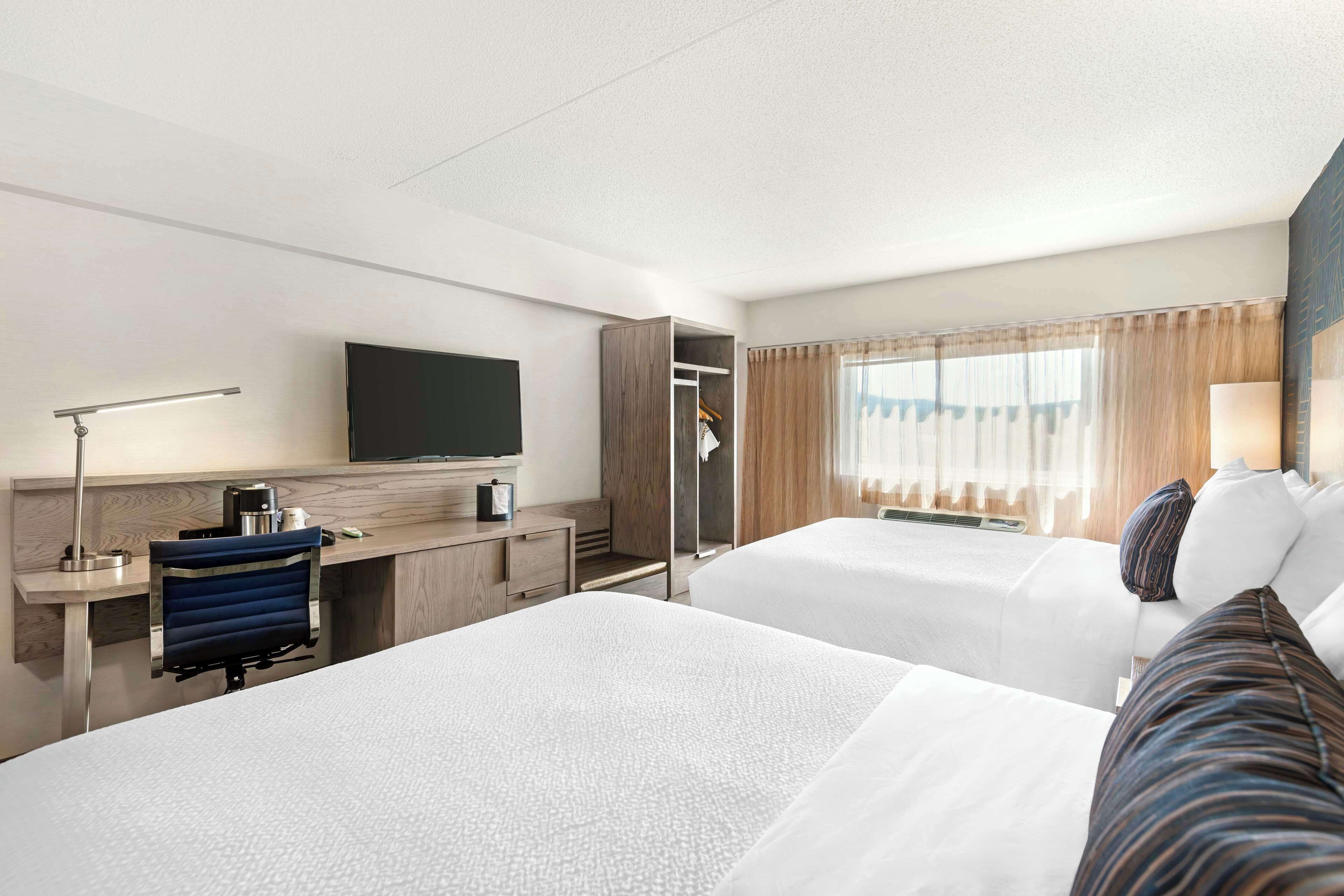 A hotel room with two beds, a desk with a computer, a TV, and a wardrobe.
