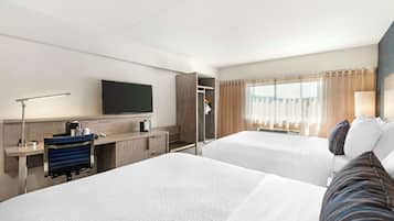 Quarto de hotel com duas camas, uma mesa de escritório, um computador, uma televisão e um guarda-roupa.
