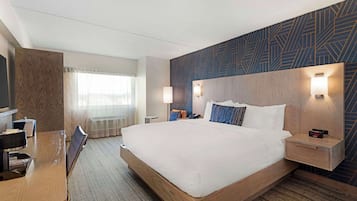 Une chambre d’hôtel avec un grand lit, un bureau avec une chaise, une télévision et une lampe de bureau.