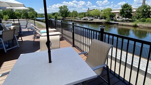 Un patio al aire libre con una mesa y sillas, un paraguas grande, y vistas a un río con un puente y edificios al fondo.
