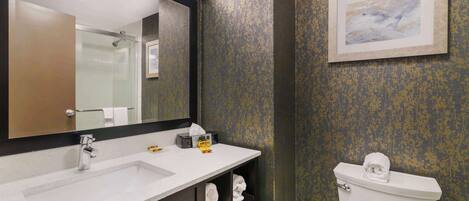 Une salle de bain avec un lavabo blanc, un miroir, des toilettes et une œuvre d’art encadrée accrochée au mur.