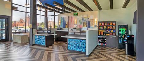 Un intérieur moderne avec un parquet en chevrons, un comptoir d’accueil, un distributeur automatique et une vue sur un bâtiment à l’extérieur.