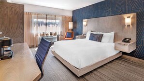 Una habitación de hotel con una cama grande, un escritorio, una silla, una mesita de noche con teléfono y una pared con diseños geométricos.