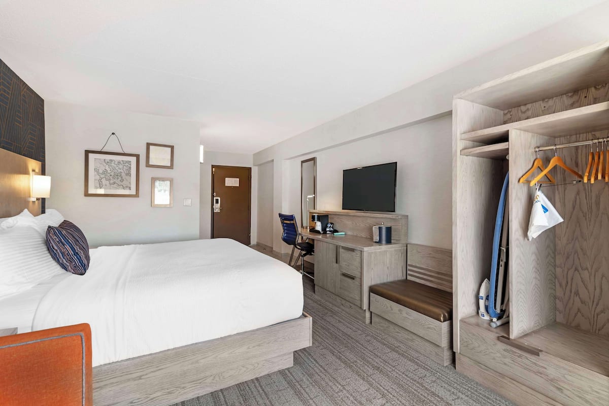 A hotel room with a bed, desk, TV, and a closet with hangers.
