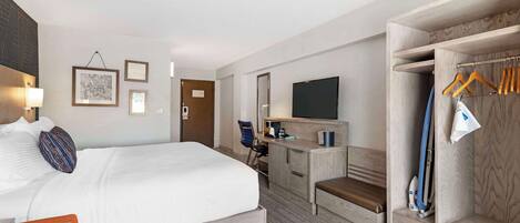 Habitación de hotel con cama, escritorio, televisión y armario con perchas.
