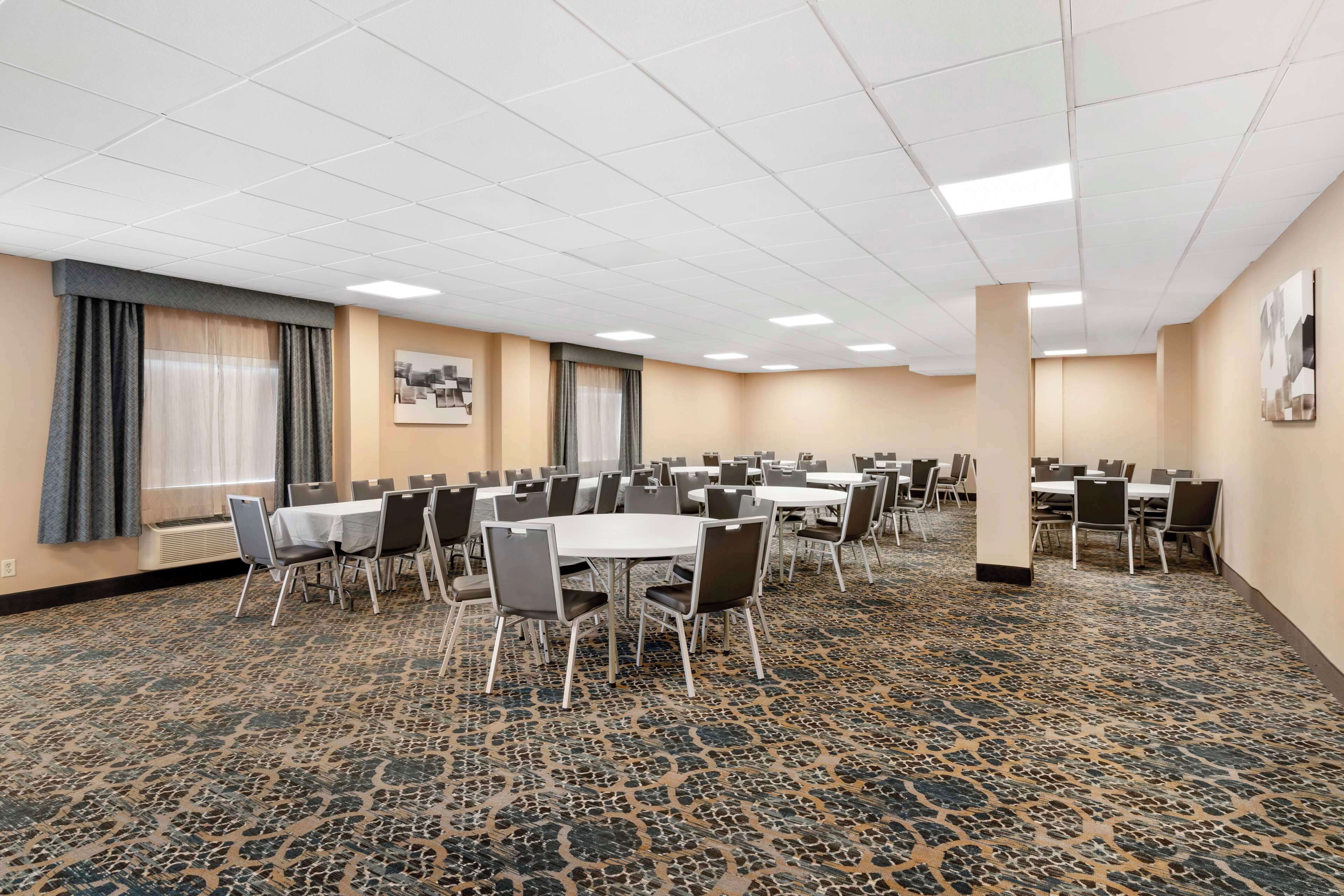 A conference room with multiple tables and chairs, carpeted floor, and large windows with curtains.