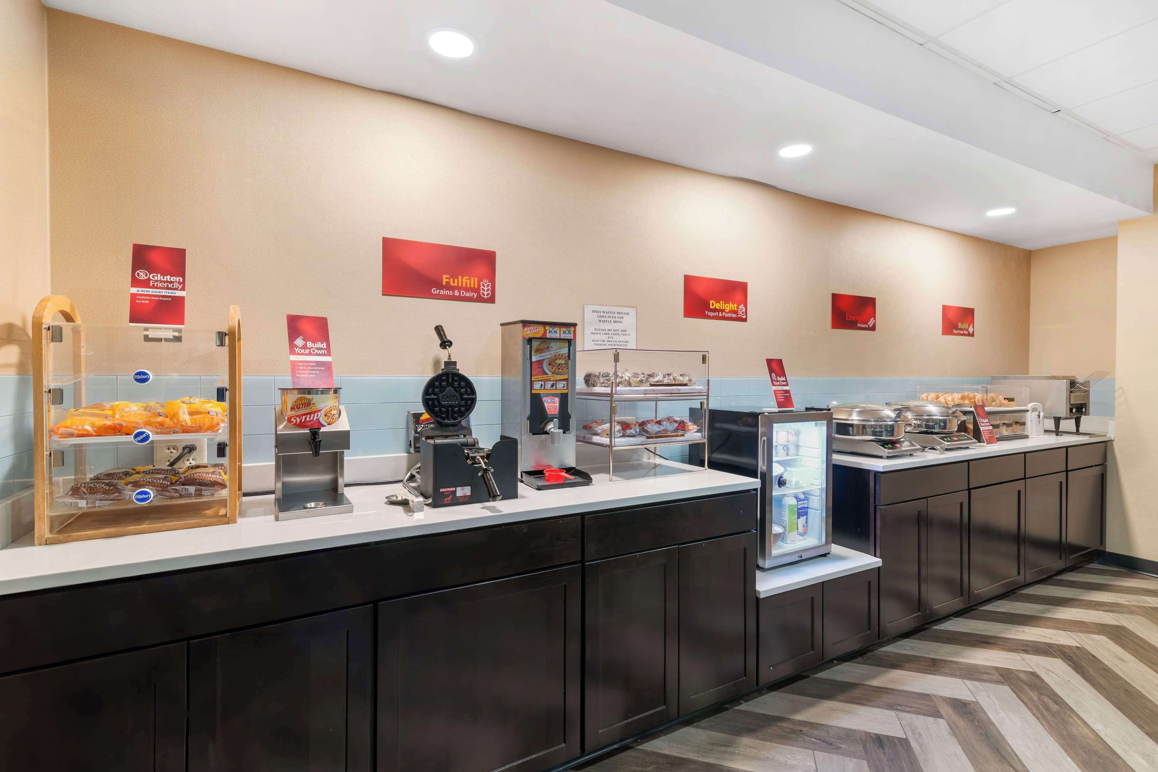 Una barra de desayuno con diferentes alimentos, una máquina de café y una vitrina.