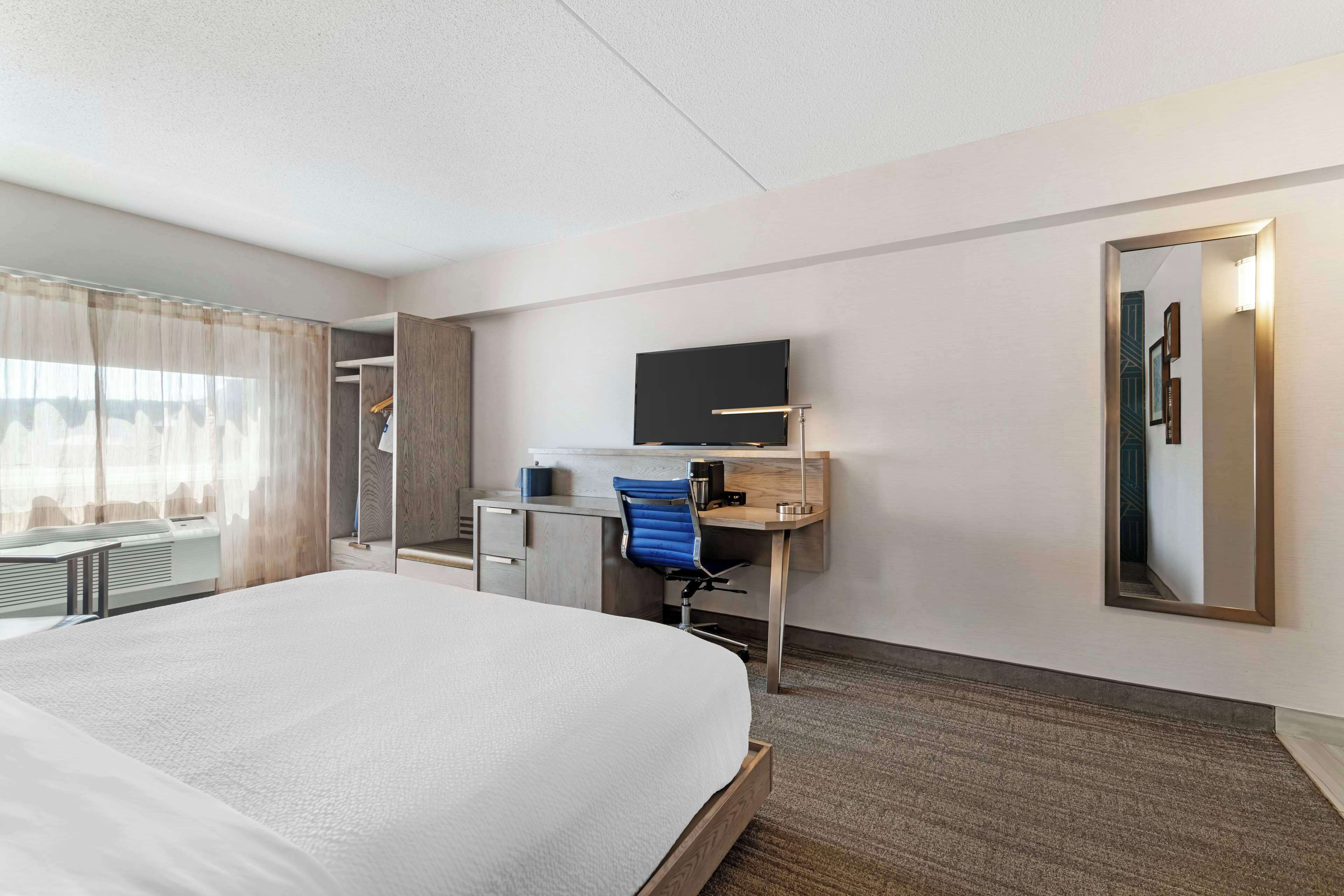 A hotel room with a large bed, a desk with a chair, a flat-screen TV, and a large mirror.