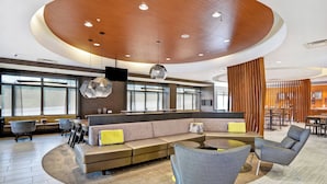 Un hall d’hôtel moderne avec un plafond en bois incurvé, un espace salon doté de canapés et de fauteuils, et un bar avec un comptoir et des tabourets.