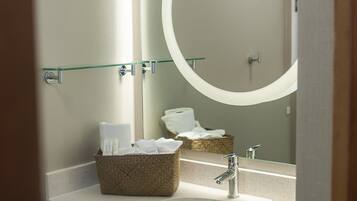 A bathroom with a glass shelf holding towels, a wooden vanity, a sink, and a large mirror with a circular frame.